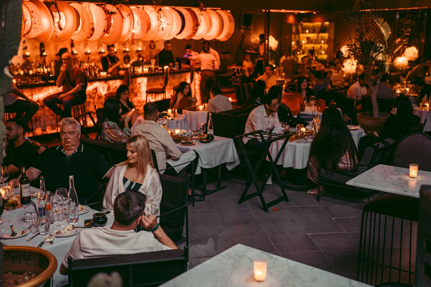 Guests at candlelit tables in the LOV dining room in Founty, with the bar lit behind them